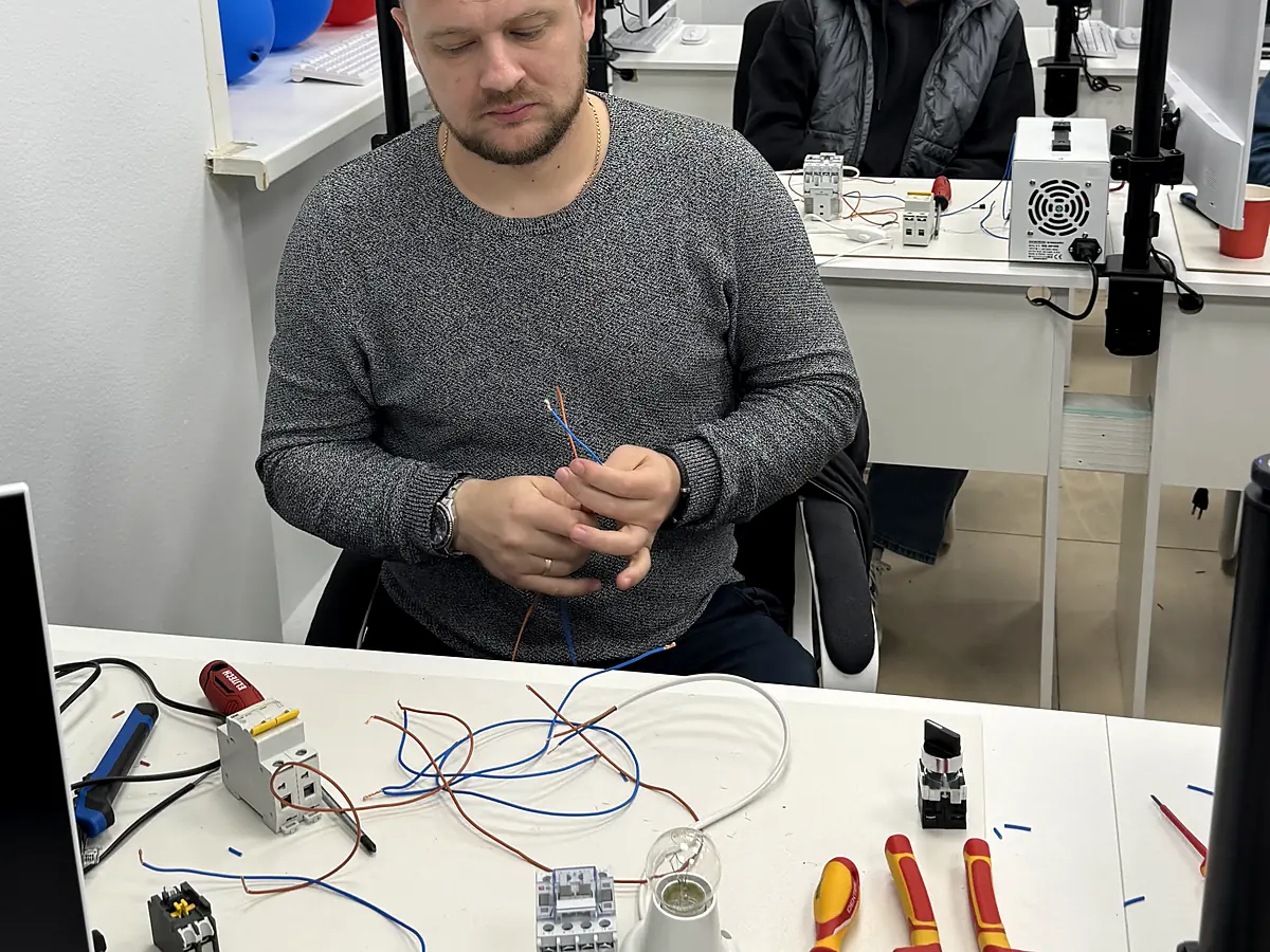Ученик за своим рабочим местом разделывает провод: автомат, пускатель, патрон и инструмент на столе
